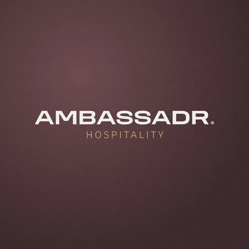 Logo AMBASSADR Hospitality blanc et doré sur un fond velours prune