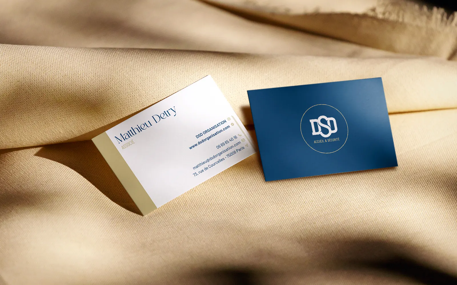 Cartes de visite DSD Organisation bleu roi et sable d'or posées sur un drapé
