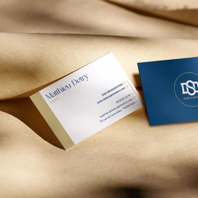 Cartes de visite DSD Organisation bleu roi et sable d'or posées sur un drapé