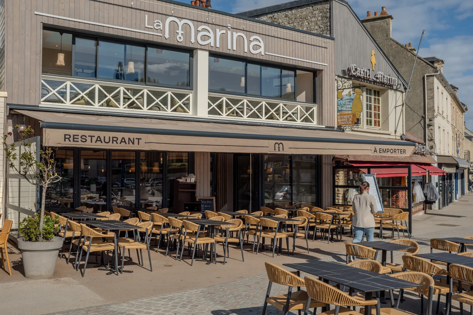 Façade bardée de bois du restaurant La Marina : enseigne en lettres blanches, lambrequin « Restaurant – À emporter », terrasse