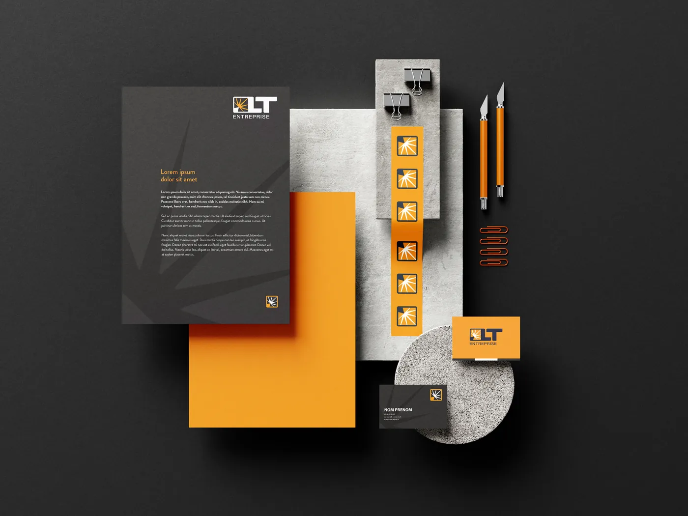 Papeterie LT Entreprise sur fond sombre : papier à en-tête, feuille orange, planche d'autocollants, cartes de visite, cutters