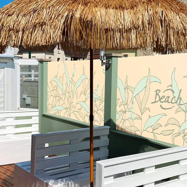 Bâche de terrasse Ô Beach illustrée de feuillages, sous un parasol en paille