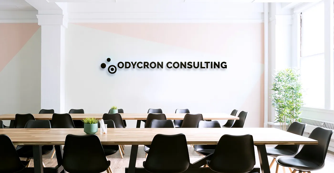 Salle de réunion lumineuse, longues tables et chaises noires, logo Odycron Consulting en lettres noires sur le mur blanc