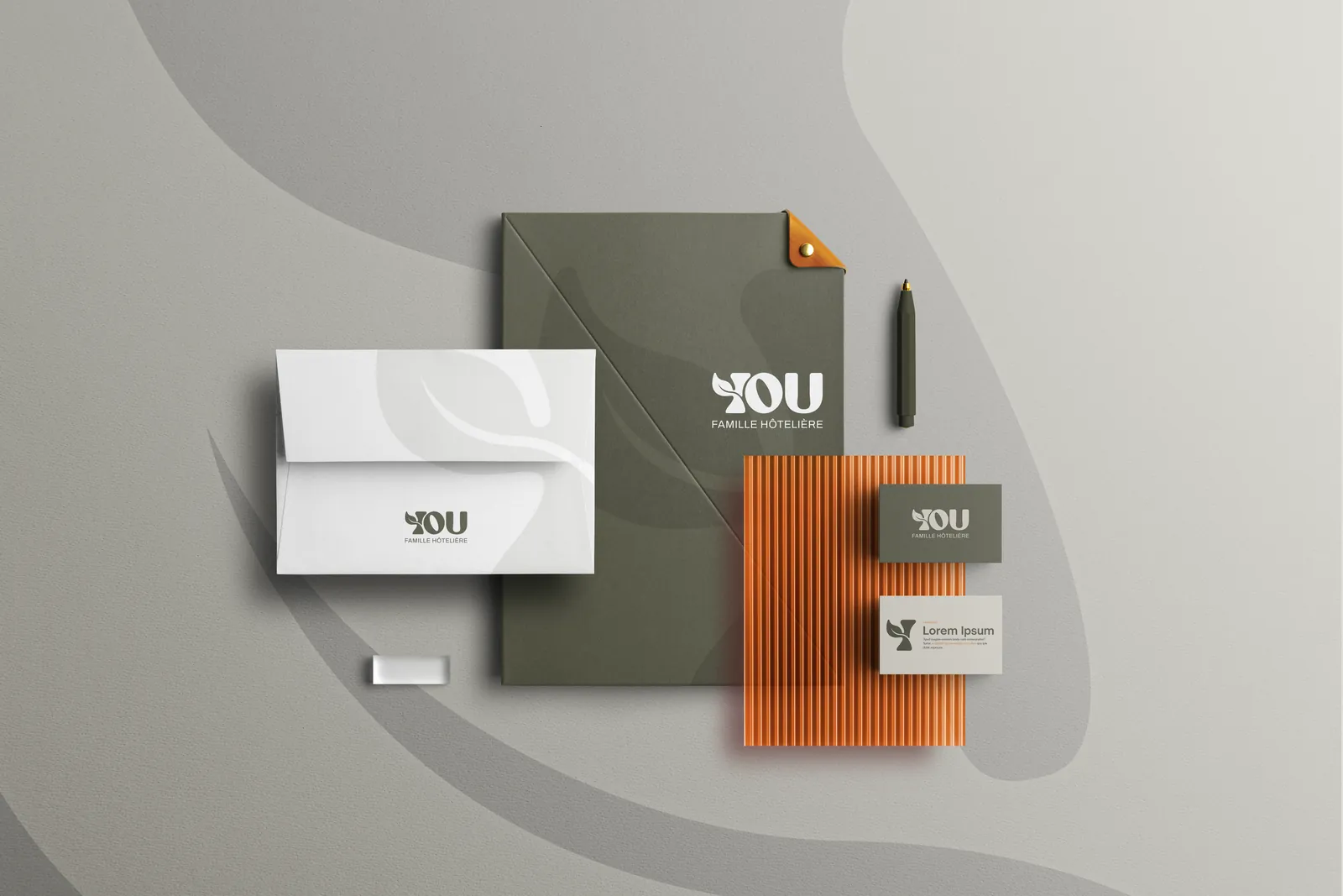 Papeterie YOU Famille Hôtelière vue du dessus : chemise vert olive, enveloppe blanche, cartes, plaque orange cannelée et stylo