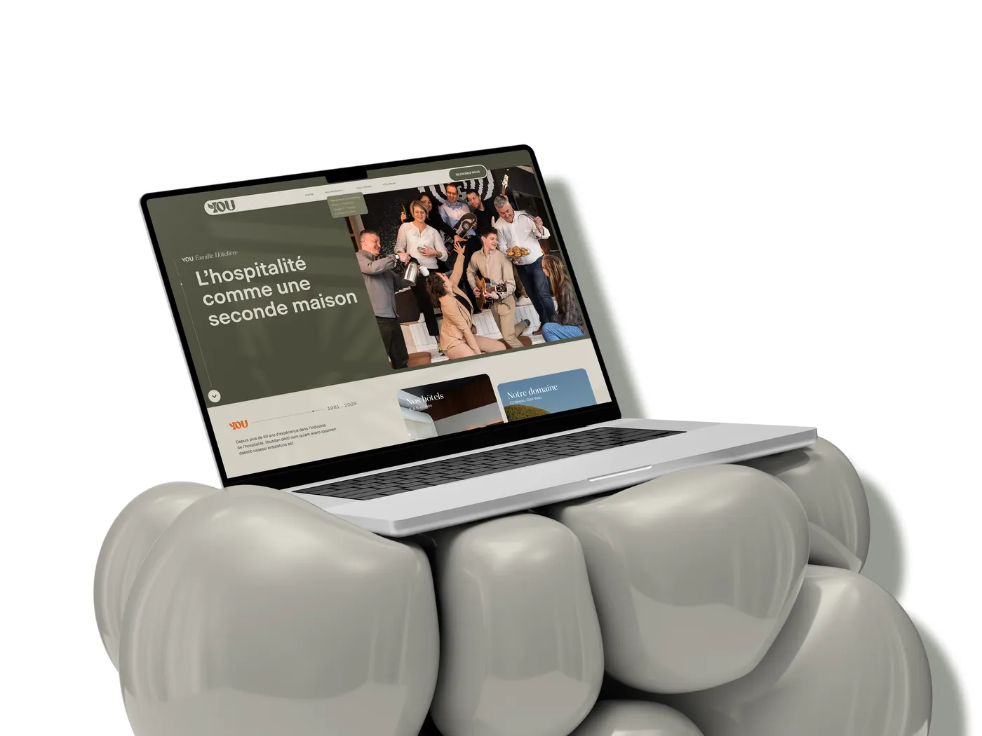 Ordinateur portable posé sur des coussins gris : page d'accueil « L'hospitalité comme une seconde maison » avec photo d'équipe